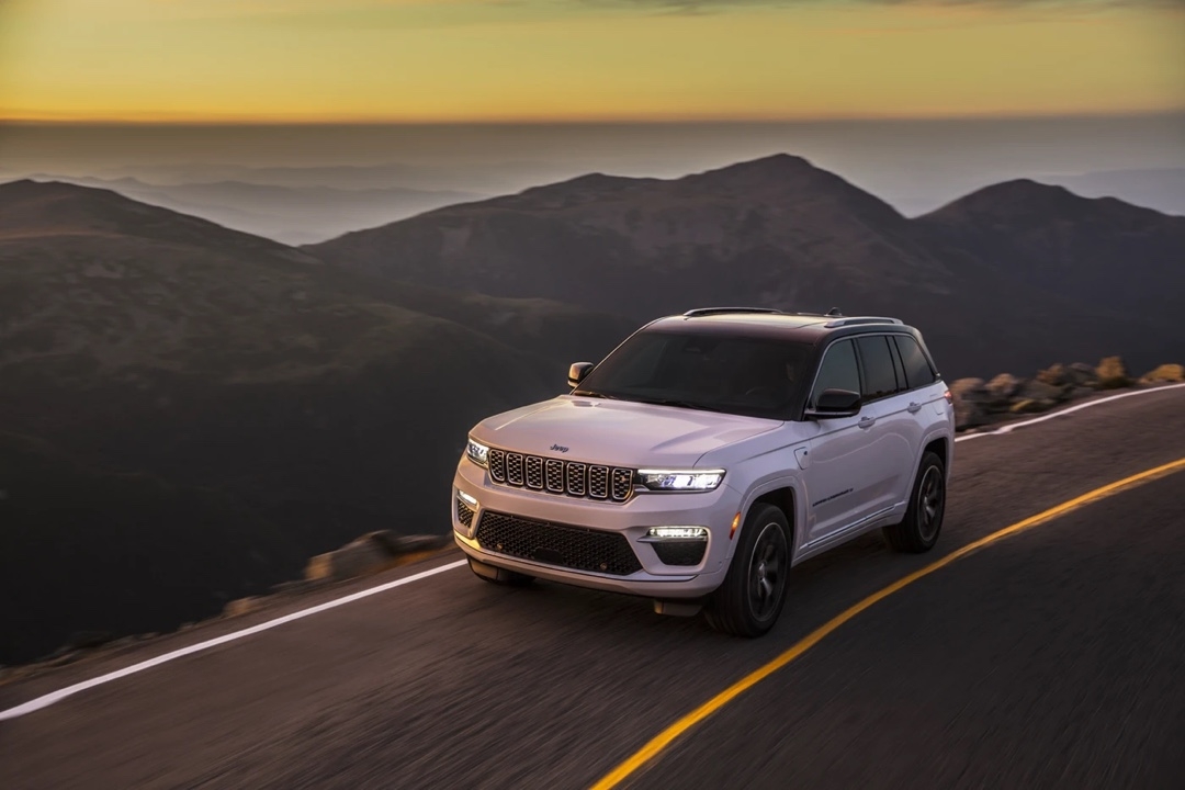 Jeep Grand Cherokee 4xe 2025 blanc roulant sur une route de montagne au coucher du soleil.