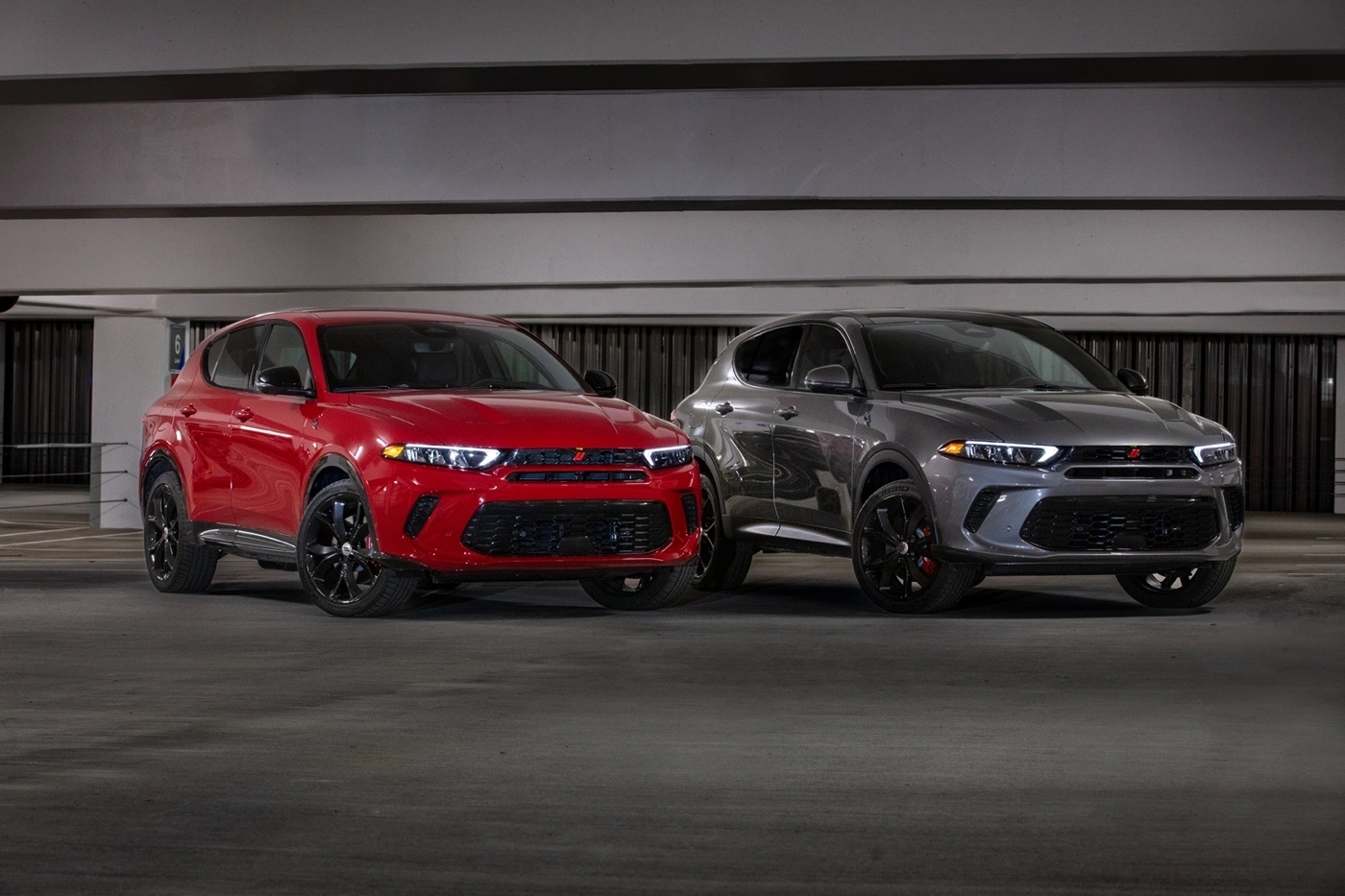 Deux Dodge Hornet GT 2025, rouge et gris, stationnés côte à côte dans un stationnement intérieur.