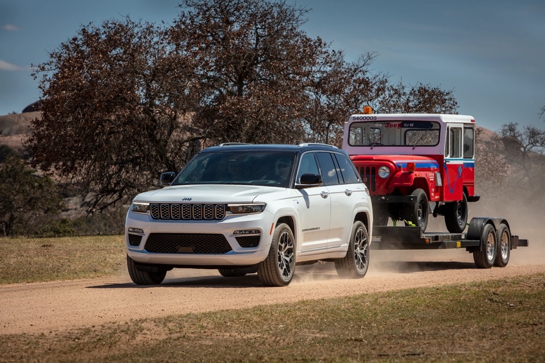 Jeep Grand Cherokee 4xe tirant une remorque avec un vieux modèle Jeep rouge et bleu.